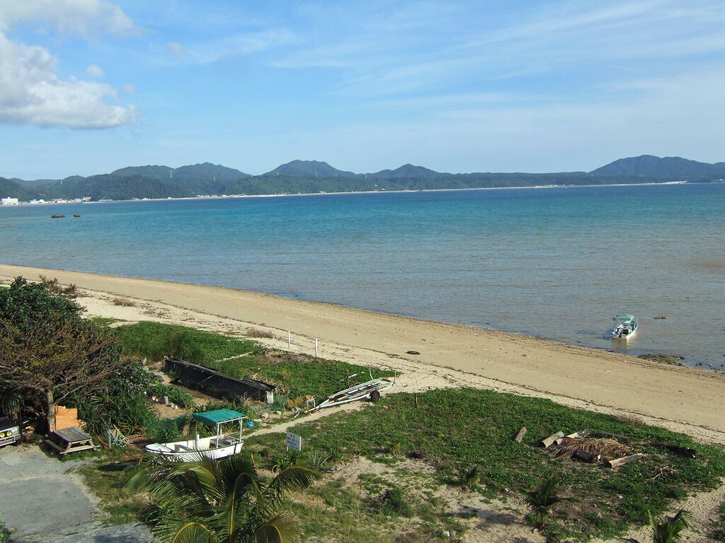 A beach with a boat, a small hut, and mountains in the background.