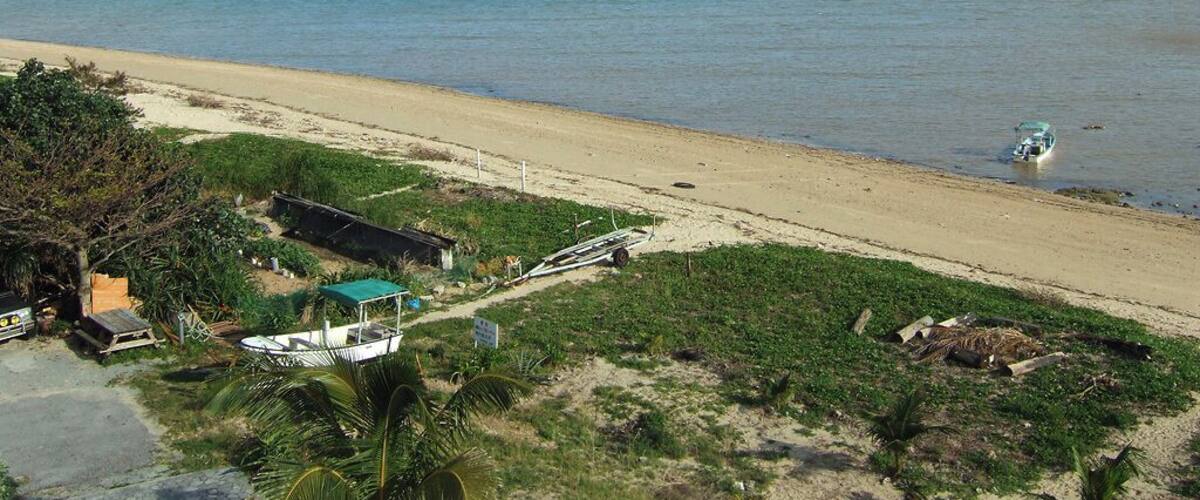 A beach with a boat, a small hut, and mountains in the background.