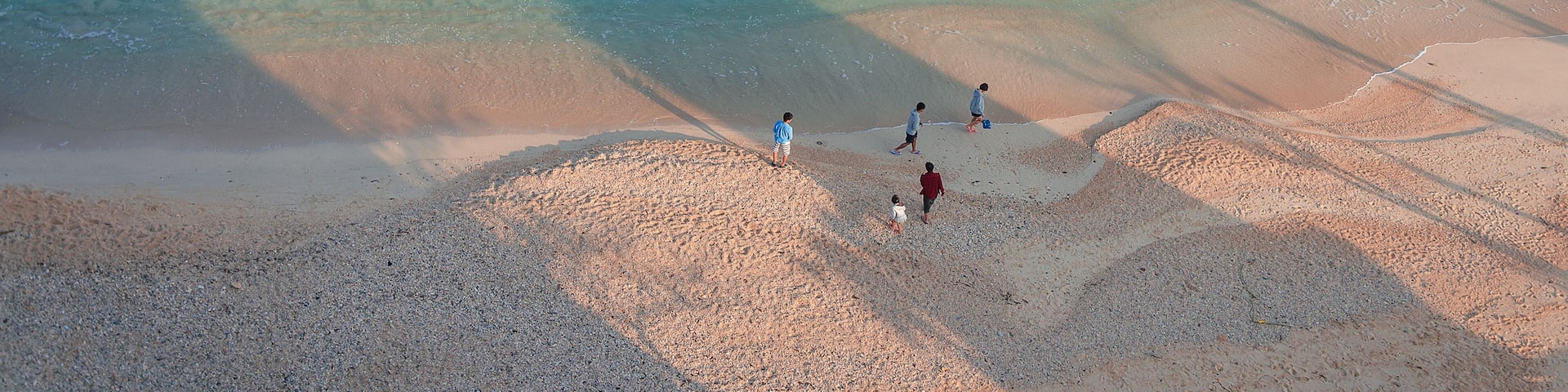 A beach with clear turquoise water and people walking on the sand.