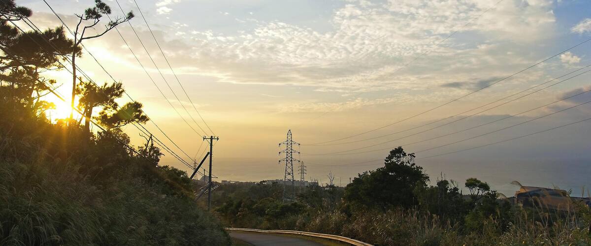 A winding road with a guardrail, surrounded by vegetation and power lines.