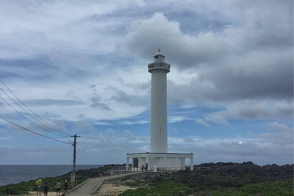 A tall white lighthouse with a small structure at its base, surrounded by rocky terrain and greenery.