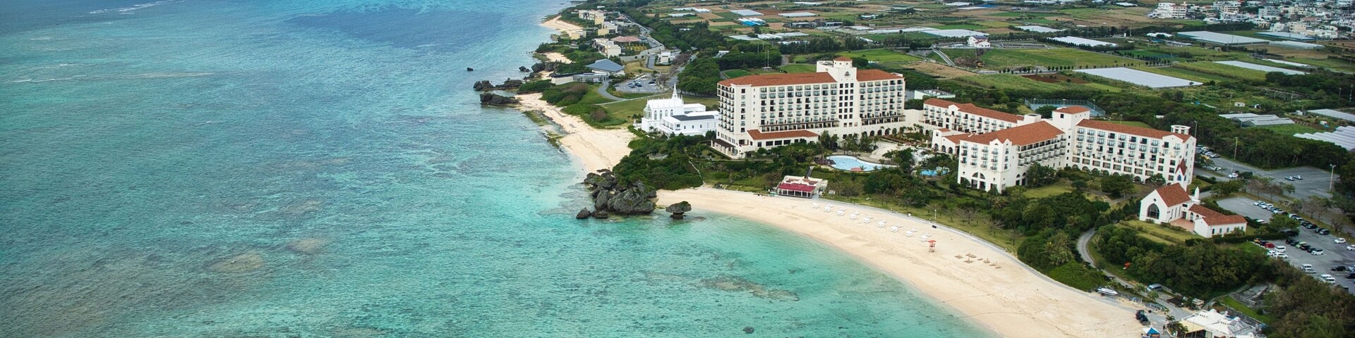 Un complejo turístico frente al mar con playa, aguas turquesas cristalinas y un gran hotel.