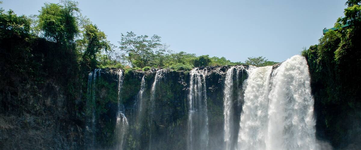 Una cascada escalonada con un primer plano rocoso y vegetación densa.