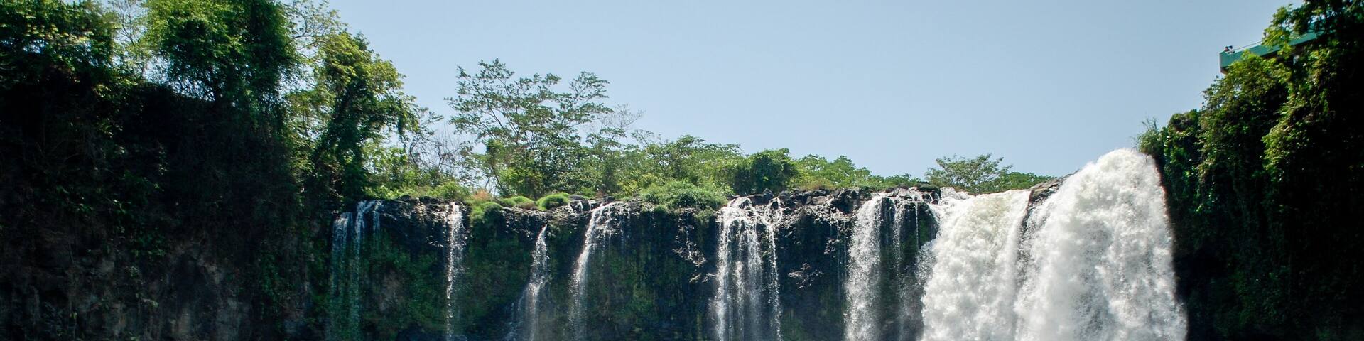 A multi-tiered waterfall with a rocky foreground and dense greenery.