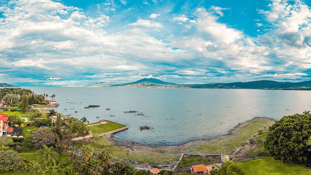 A panorama of mountains and lake with the sunset as background. Clouds and blue sky with trees and colors