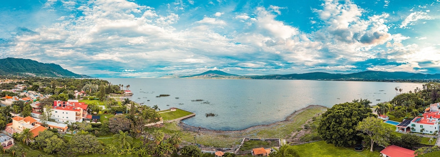 A panorama of mountains and lake with the sunset as background. Clouds and blue sky with trees and colors