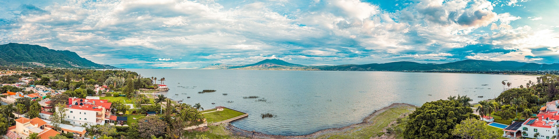 A panorama of mountains and lake with the sunset as background. Clouds and blue sky with trees and colors