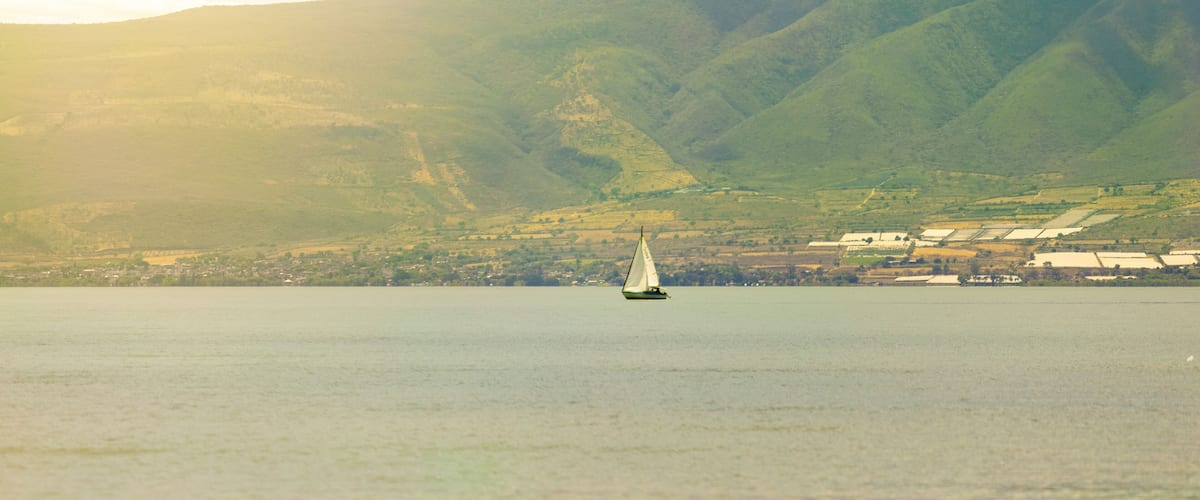 Ein Segelboot auf einem ruhigen See vor einer Bergkulisse.