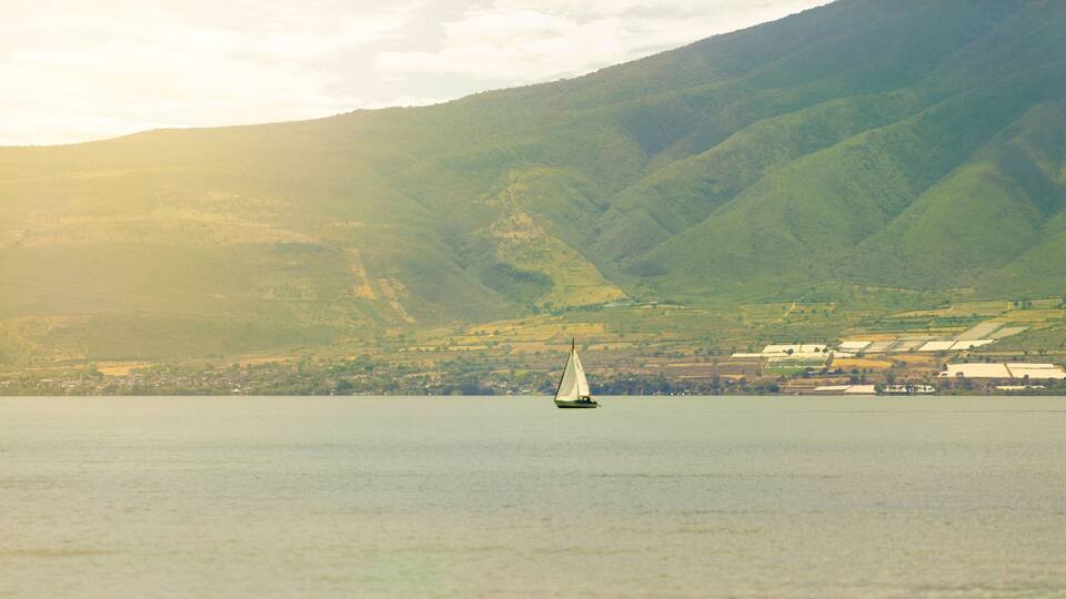 A sailboat on a calm lake with a mountainous backdrop.