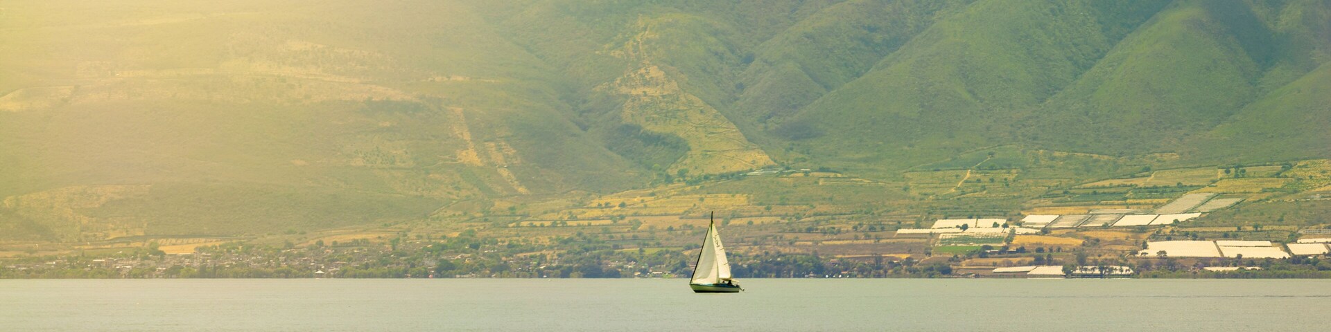 Un velero en un lago tranquilo con montañas al fondo.