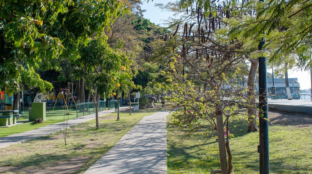 A park with a paved walkway, green grass, trees, and playground equipment.