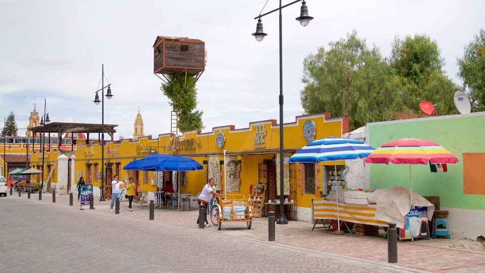 A street with yellow buildings, blue and red umbrellas, and a person riding a bicycle.