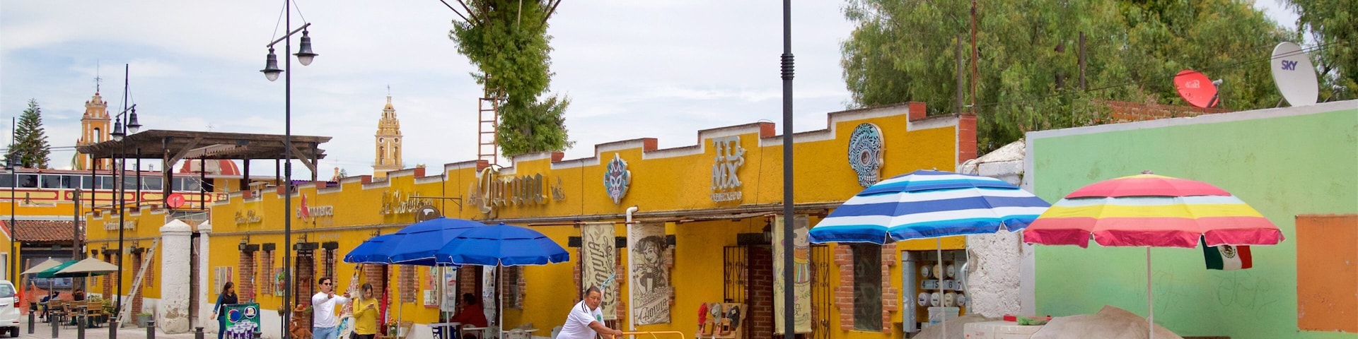 Una calle con edificios amarillos, sombrillas azules y rojas, y una persona montando en bicicleta.