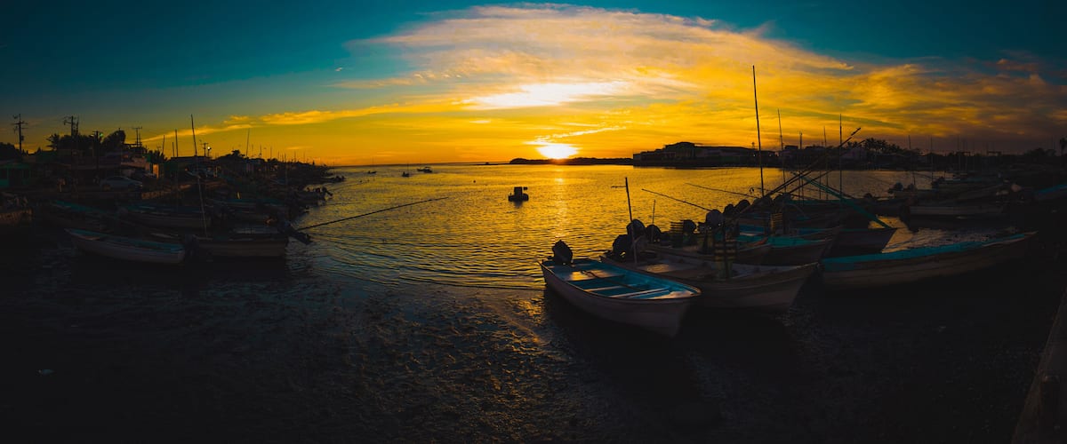 A harbor at sunset with boats docked and a calm sea.
