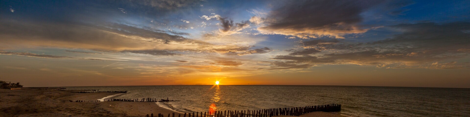 Atardecer sobre una playa con postes de madera y cielo despejado.
