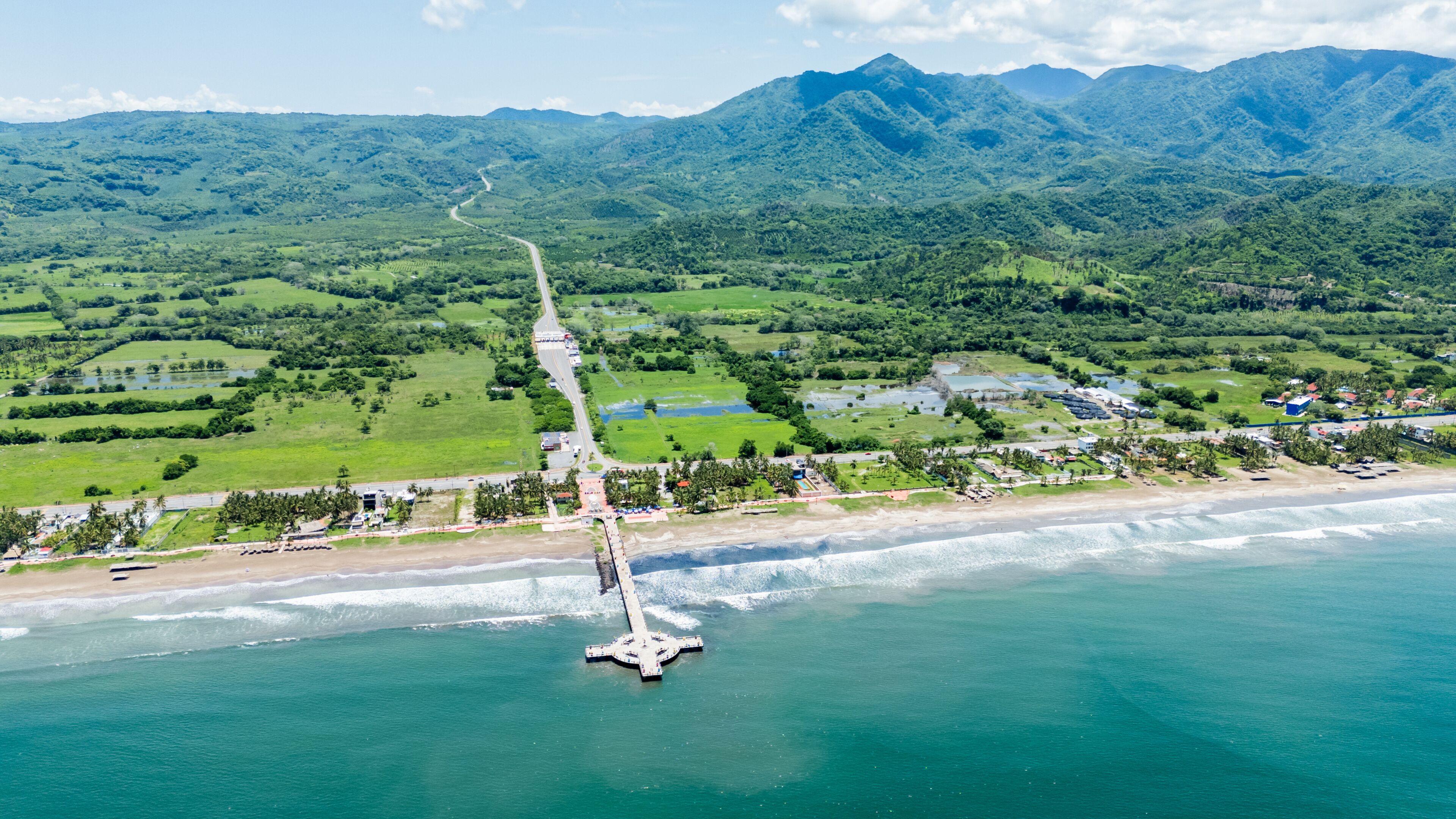 A coastal landscape with a road leading to a beach, surrounded by lush green hills and mountains.