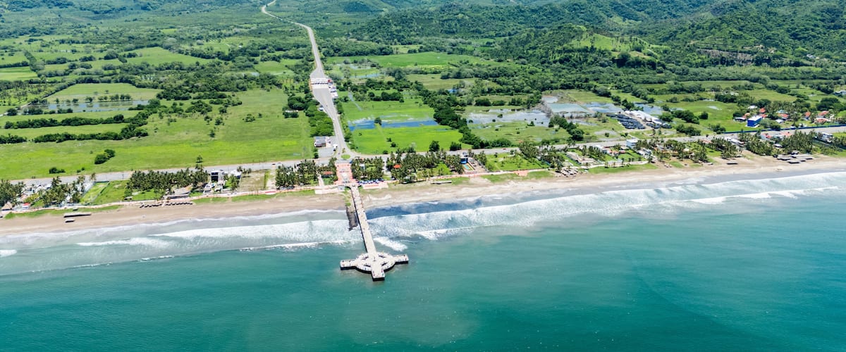 A coastal landscape with a road leading to a beach, surrounded by lush green hills and mountains.