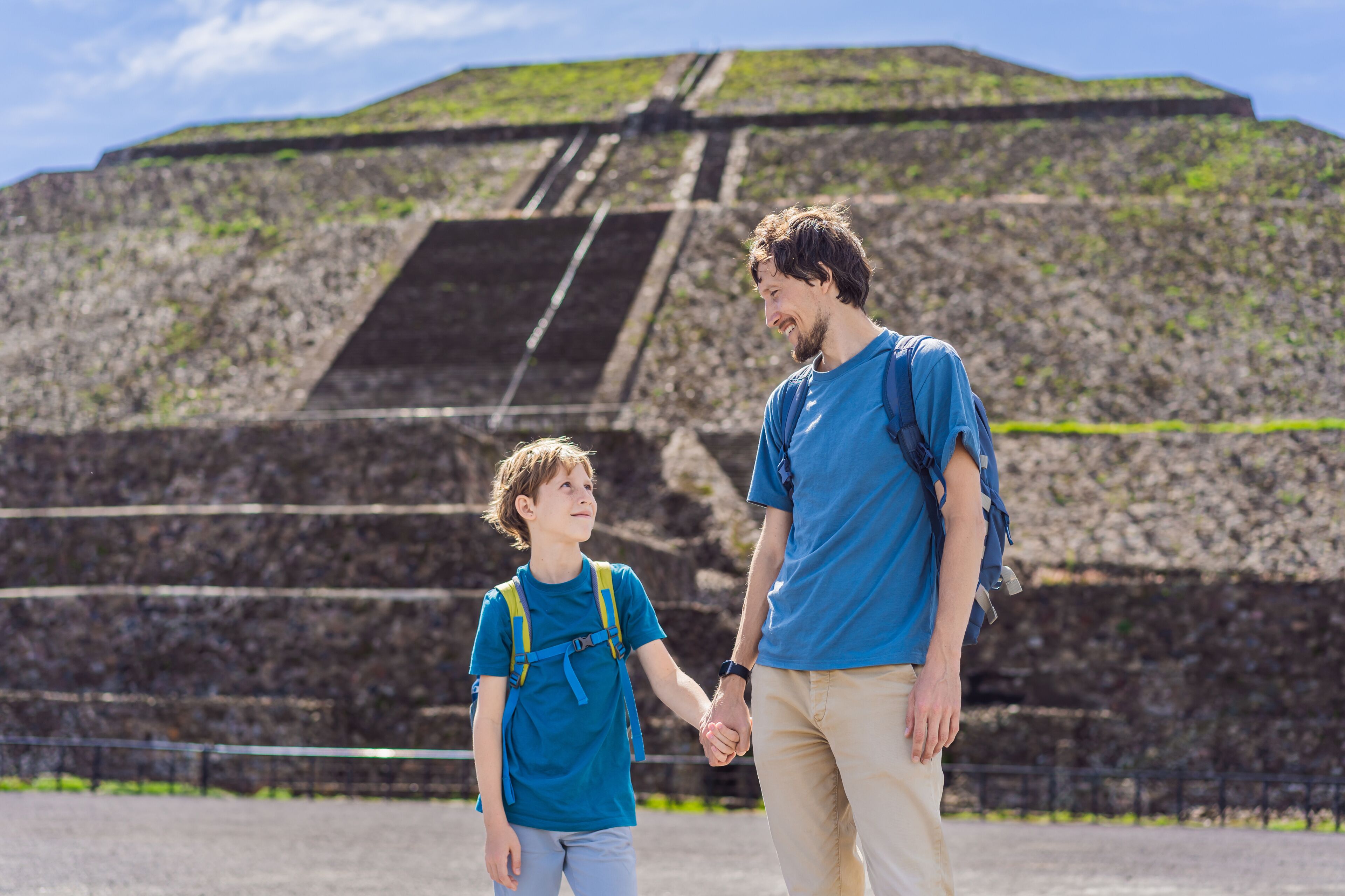 Una persona y un niño tomados de la mano frente a una gran estructura piramidal.