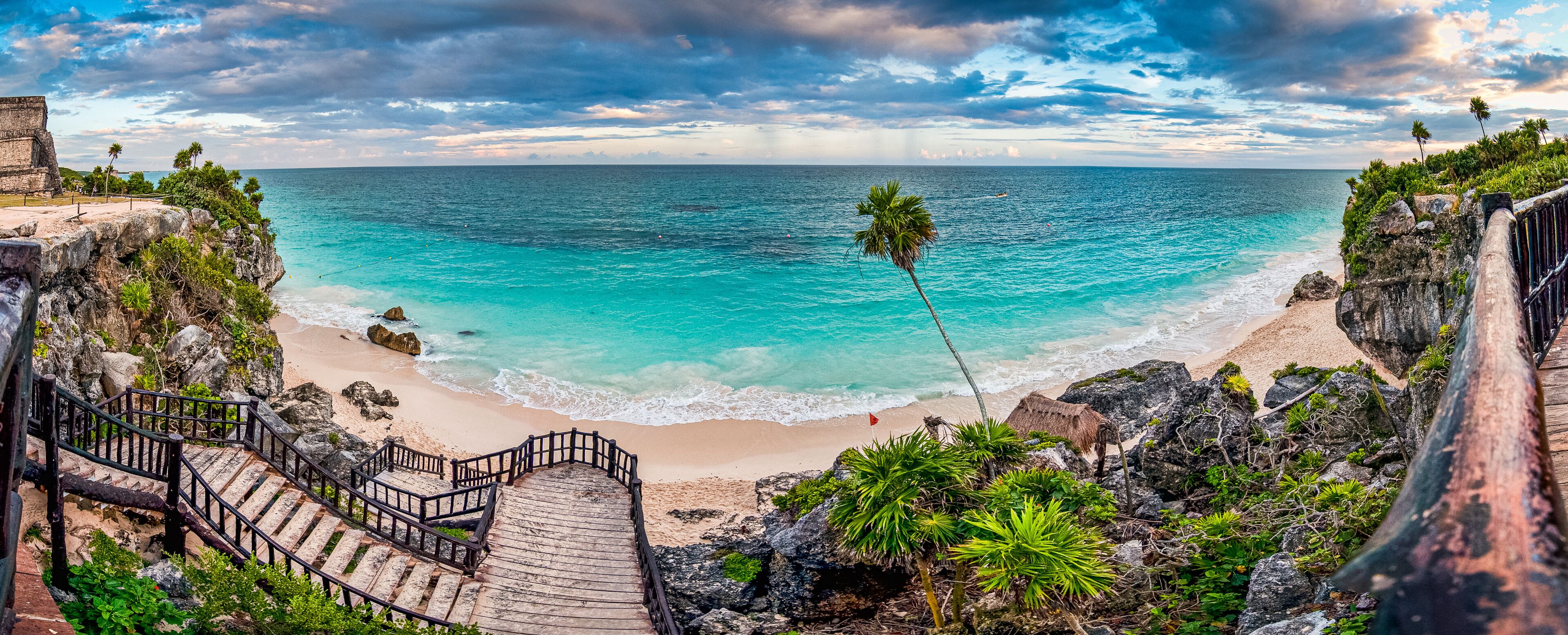 A coastal view with turquoise waters, a sandy beach, and a wooden staircase leading down to the shore.