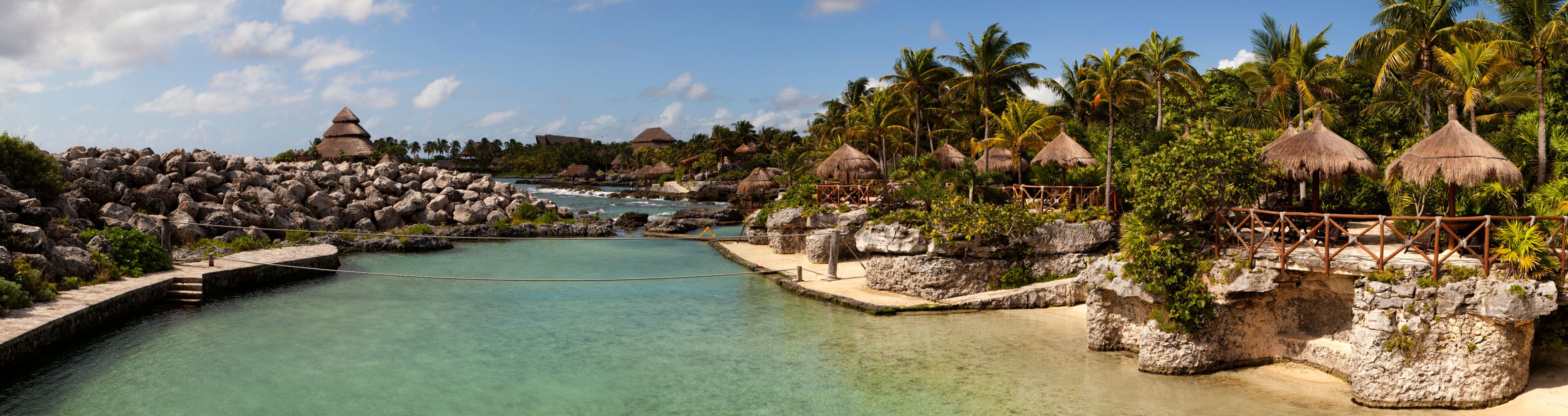 A tropical resort with clear turquoise waters, thatched-roof huts, and lush greenery.
