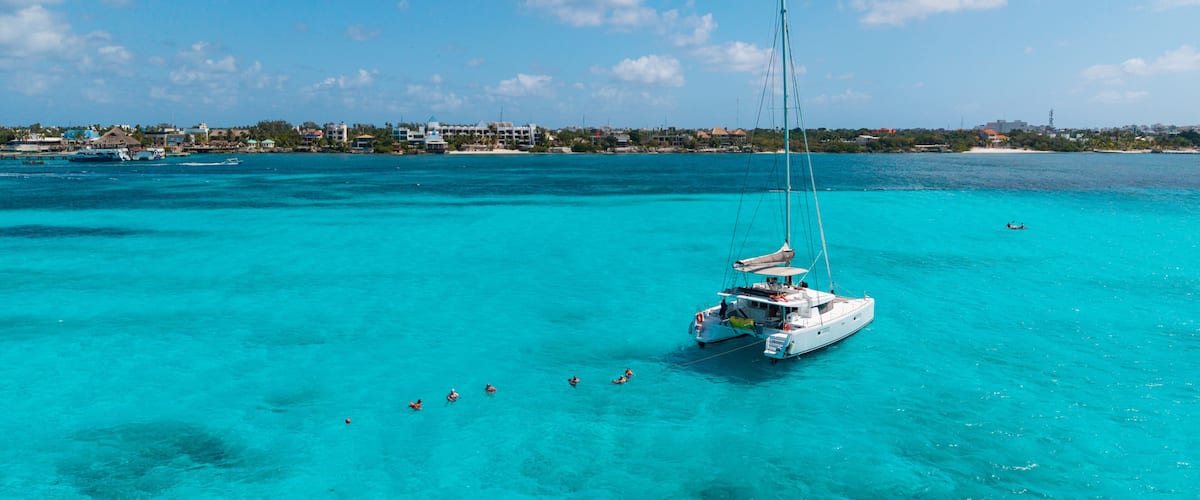 Un velero en aguas turquesas, con un pueblo costero al fondo.