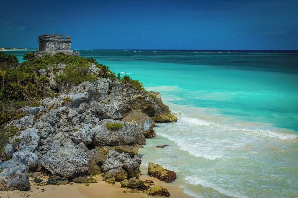 A rocky coastline with turquoise waters and a stone structure on a cliff.