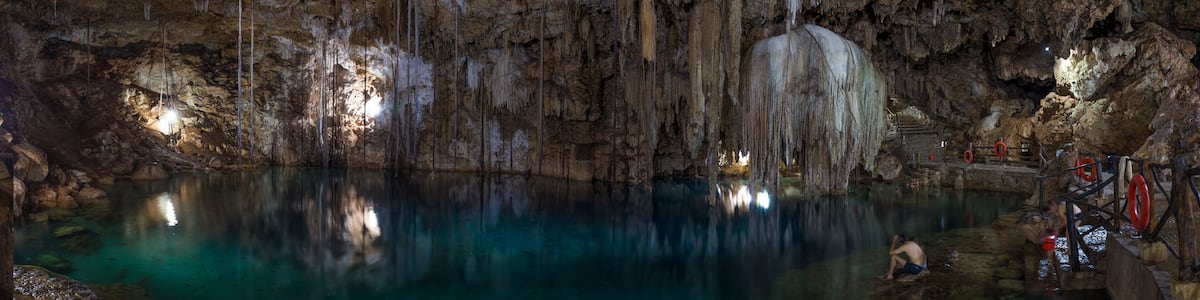 Une grotte ornée de stalactites et de stalagmites, une étendue d’eau et une personne en train d’escalader une formation rocheuse.