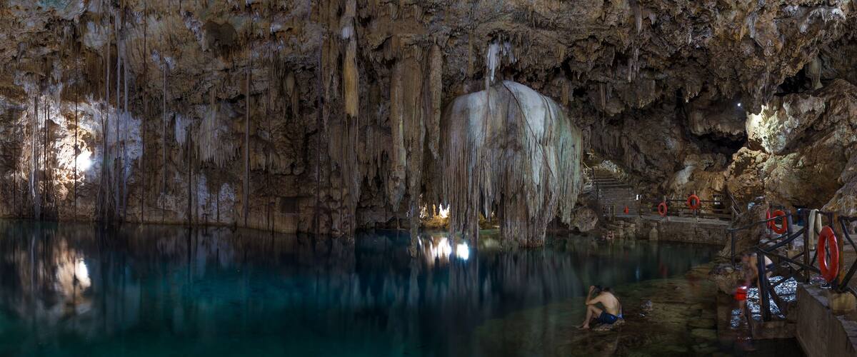 A cave with stalactites and stalagmites, a pool of water, and a person climbing a rock formation.