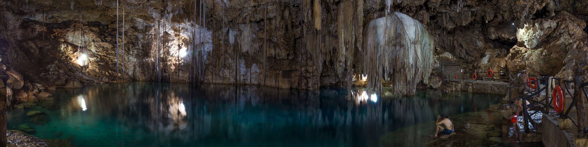 A cave with stalactites and stalagmites, a pool of water, and a person climbing a rock formation.