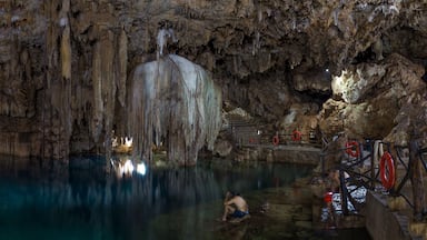 Una cueva con estalactitas y estalagmitas, un charco de agua y una persona escalando una formación rocosa.