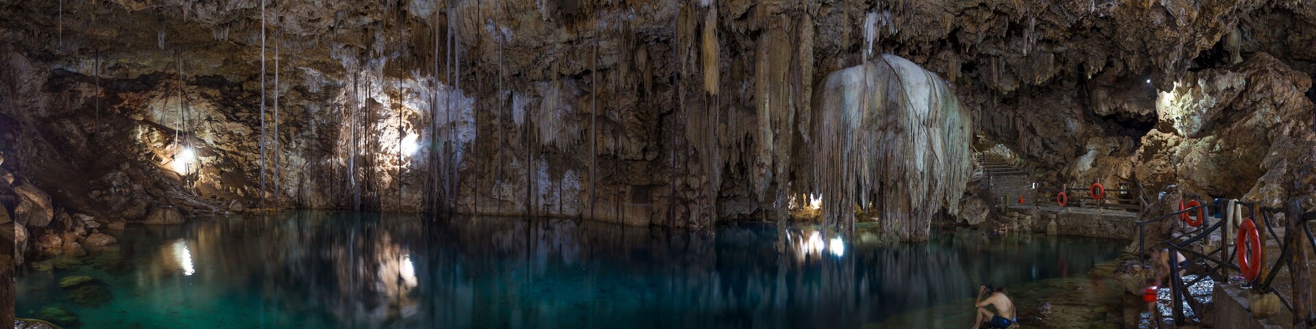 Una cueva con estalactitas y estalagmitas, un charco de agua y una persona escalando una formación rocosa.