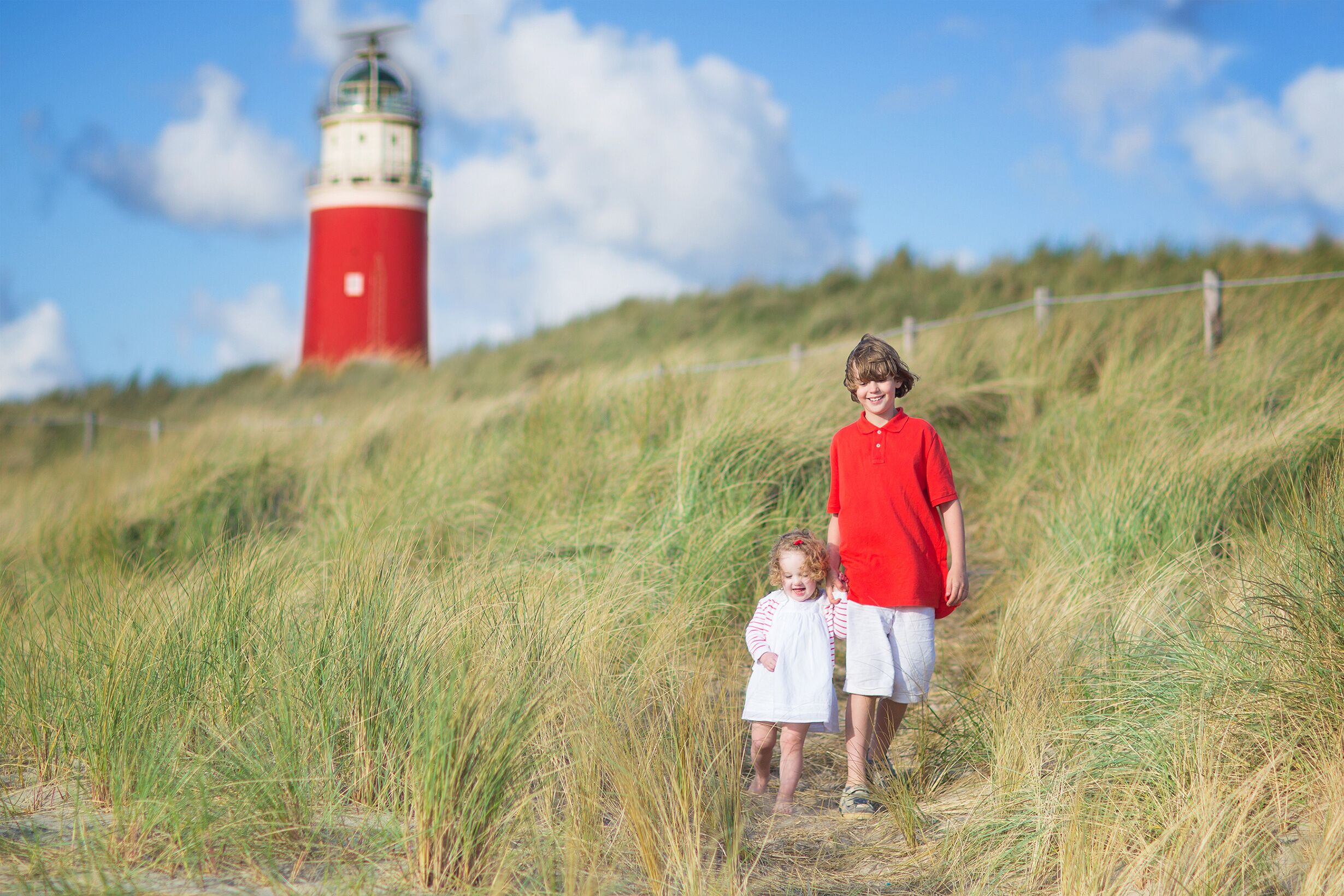 Brother and sister walking on the beach next to lighthouse