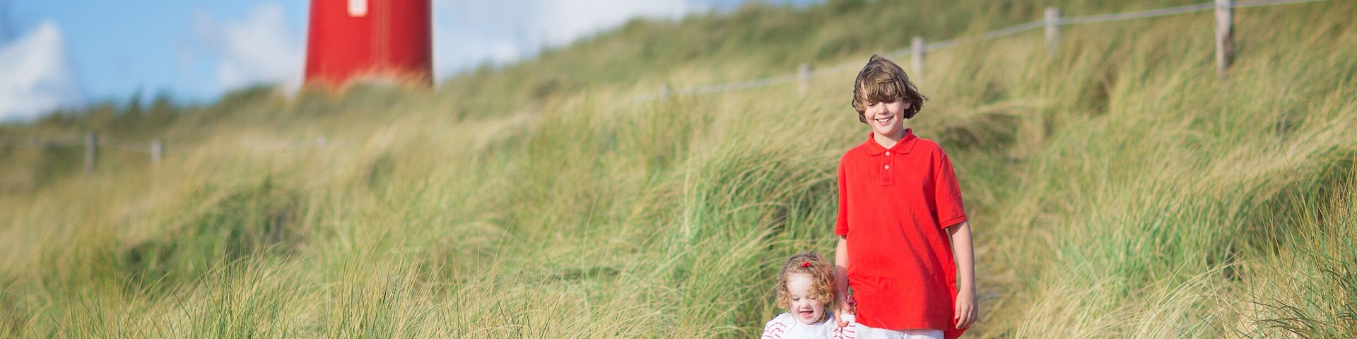 A lighthouse, a grassy hill, and a person in a red shirt.