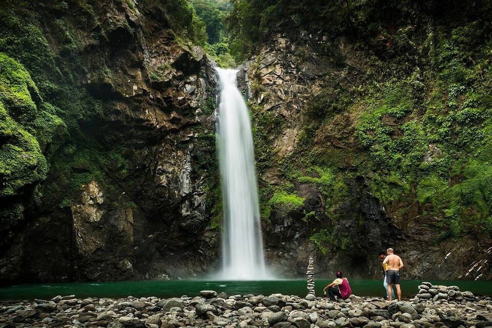Una cascada se precipita por un risco rocoso rodeado de abundante vegetación.