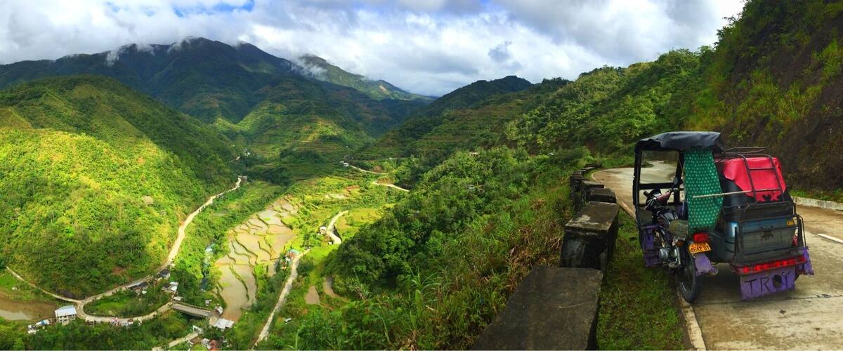A truck on a winding mountain road surrounded by lush green hills and terraced fields.