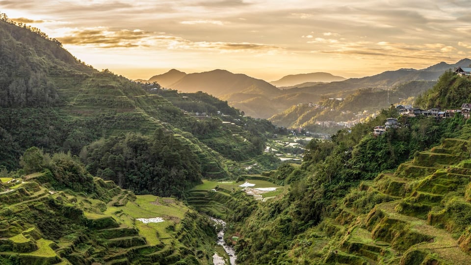 Terraced rice fields, a river, and a village nestled in a valley with mountains in the background.