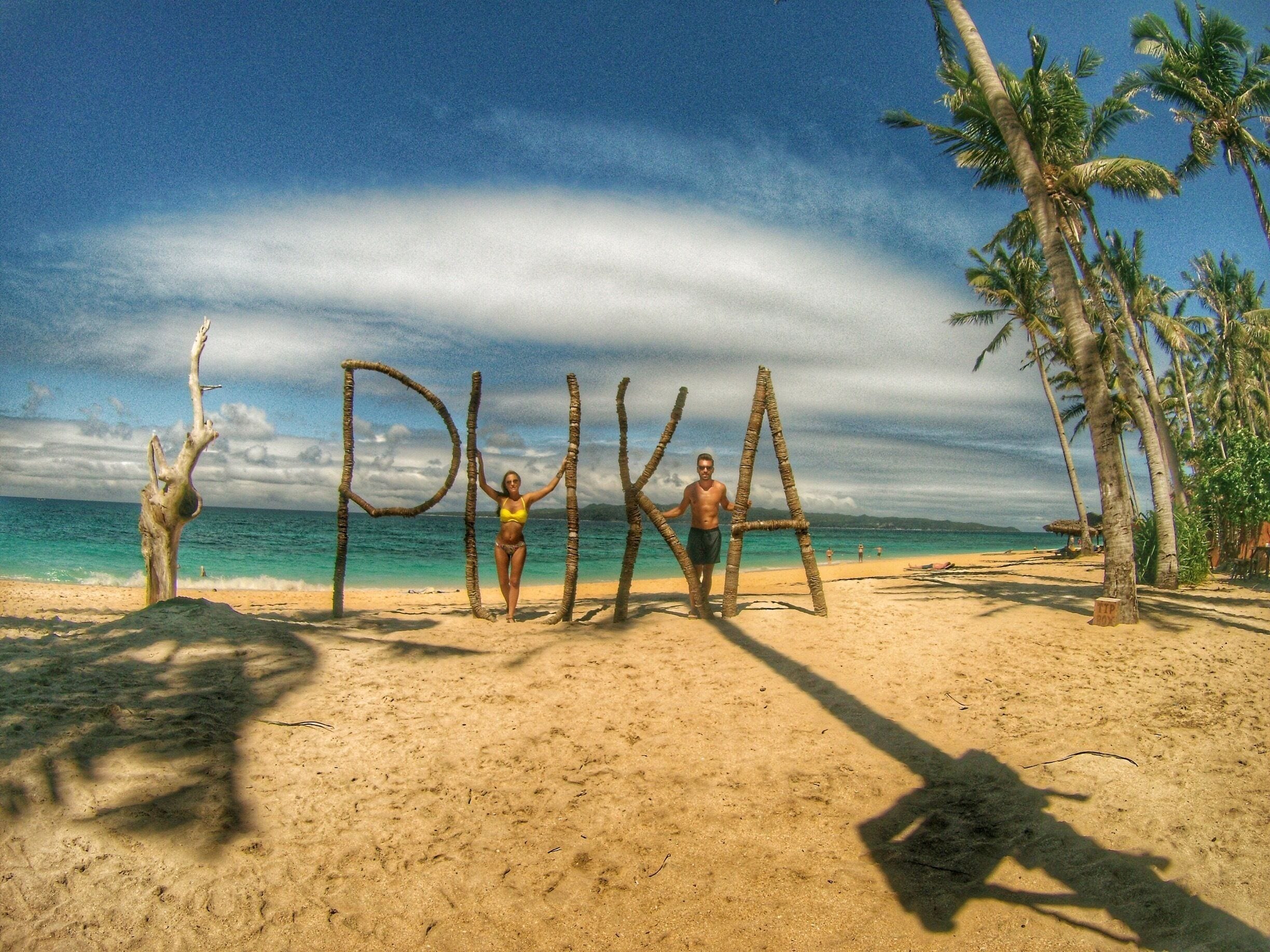 A beach with palm trees, a clear sky, and the word "PIKA" spelled out with sticks.