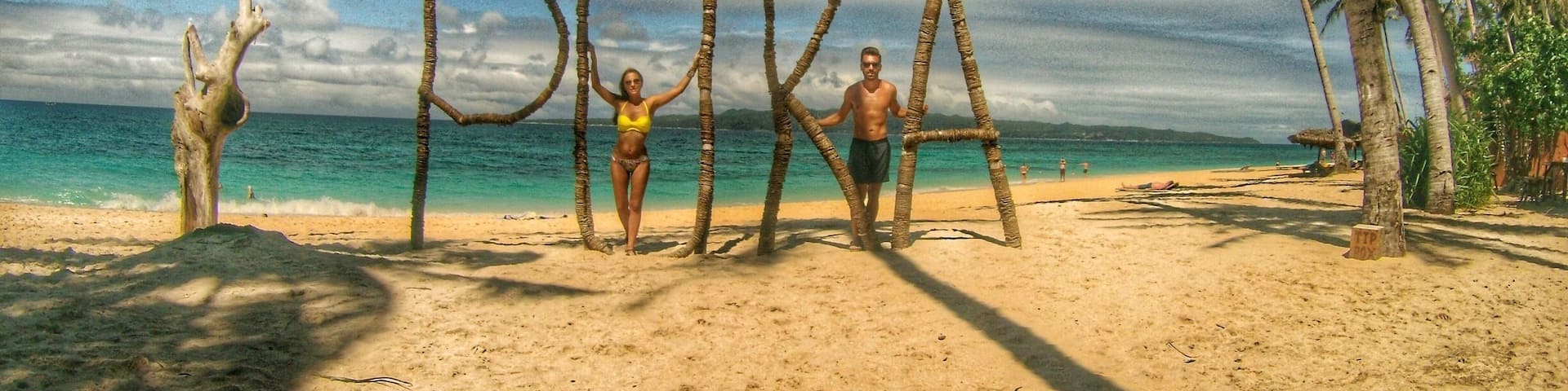 A beach with palm trees, a clear sky, and the word "PIKA" spelled out with sticks.