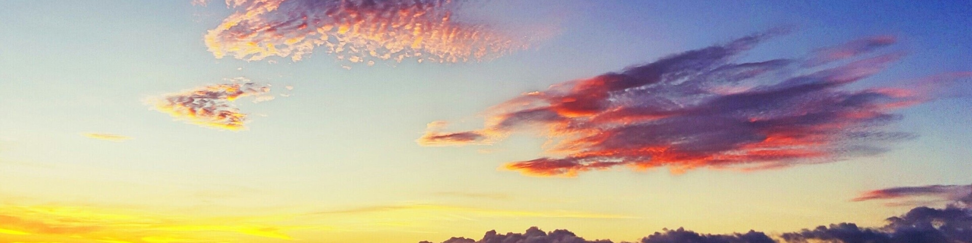 Um pôr do sol sobre uma praia com pessoas nadando e veleiros ao longe.