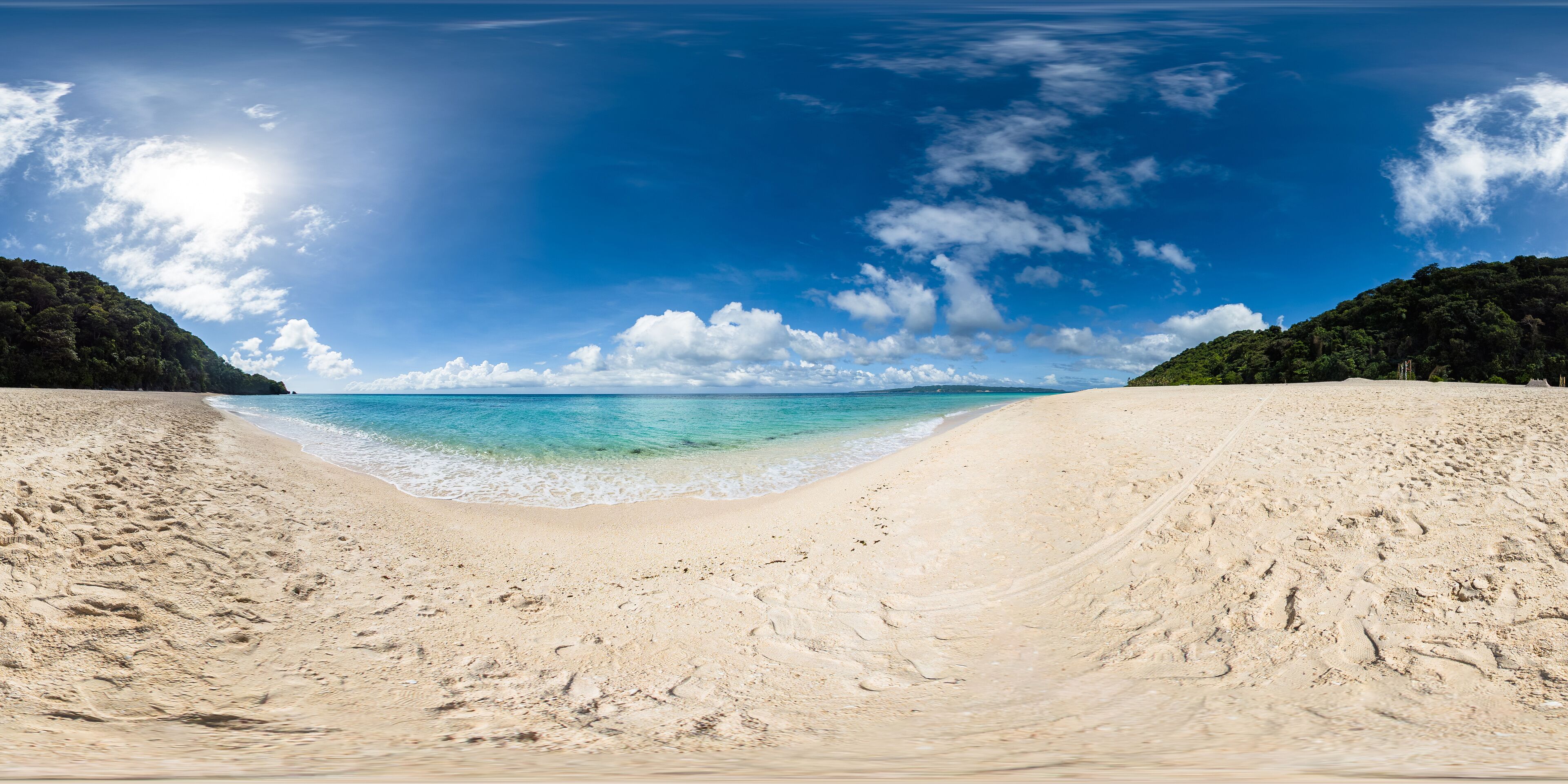 A wide sandy beach with clear turquoise water and a clear sky.