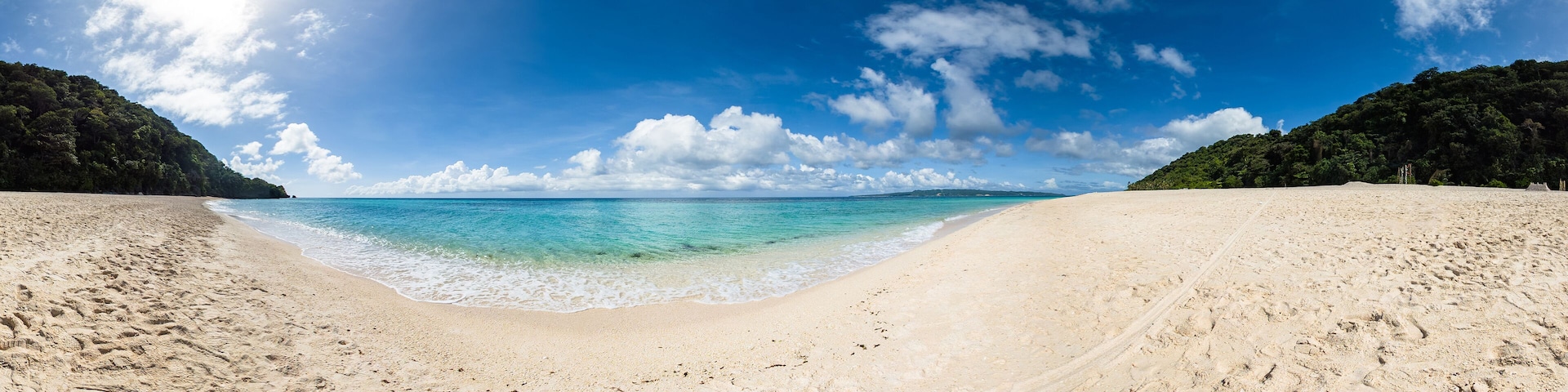 Una extensa playa arenosa con agua turquesa cristalina y un cielo despejado.