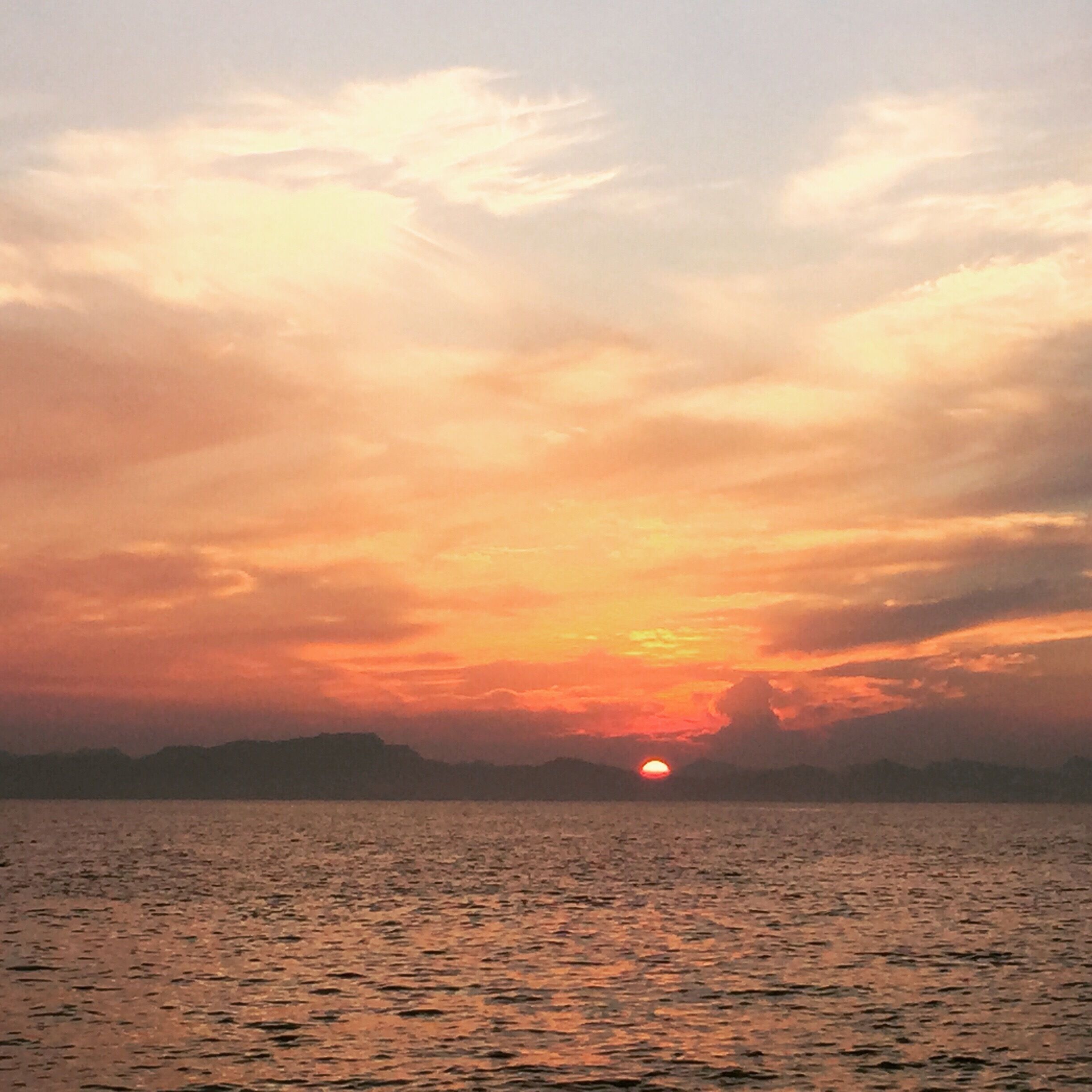 A sunset over a calm body of water with a silhouette of distant mountains.