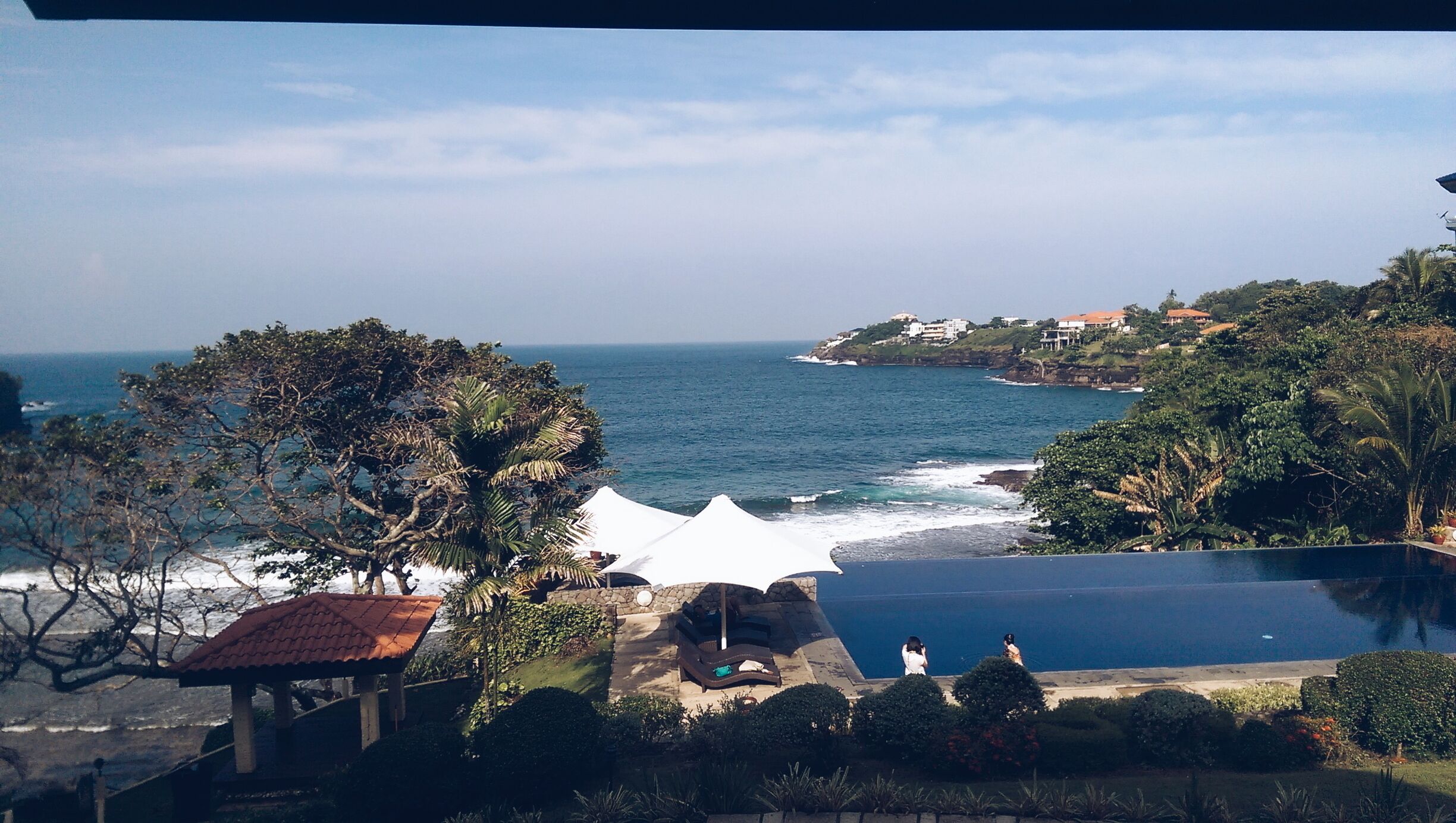 A coastal view with a swimming pool, a white tent, and a rocky shoreline.