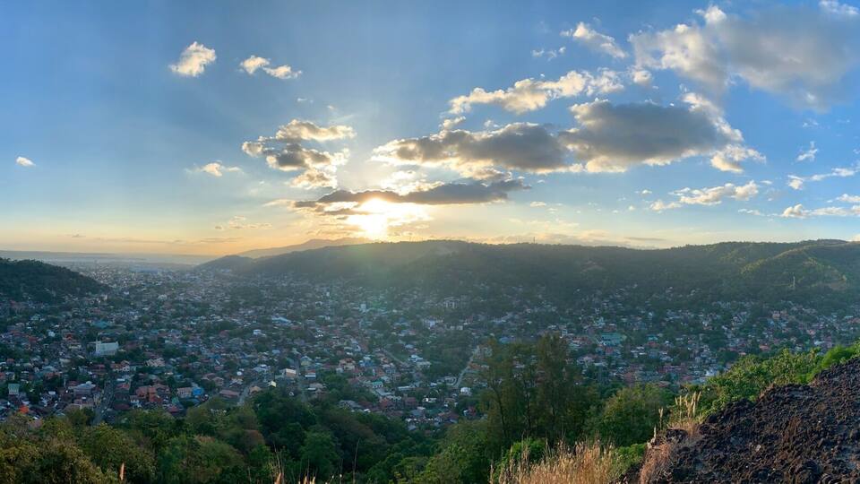 A panoramic view of a town with a mountainous backdrop, two crosses on a hill, and a clear sky.