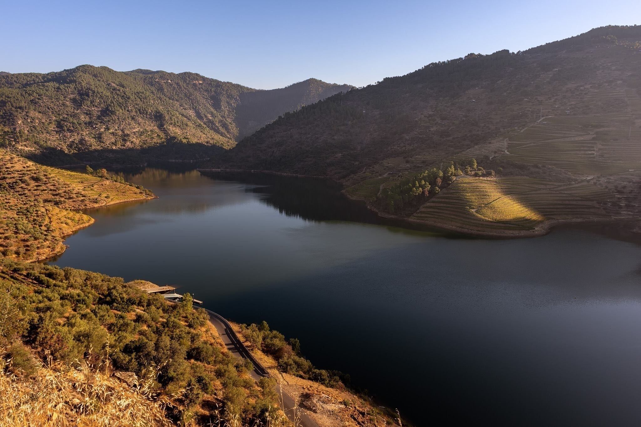 A lake surrounded by hills with a winding road and a bridge.