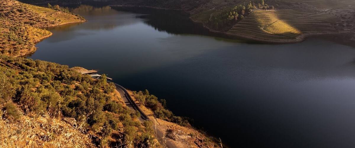 A lake surrounded by hills with a winding road and a bridge.