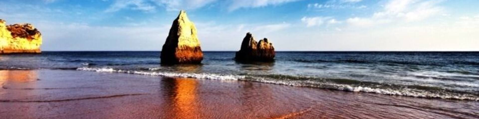 A beach with two prominent rock formations in the water and a clear blue sky.