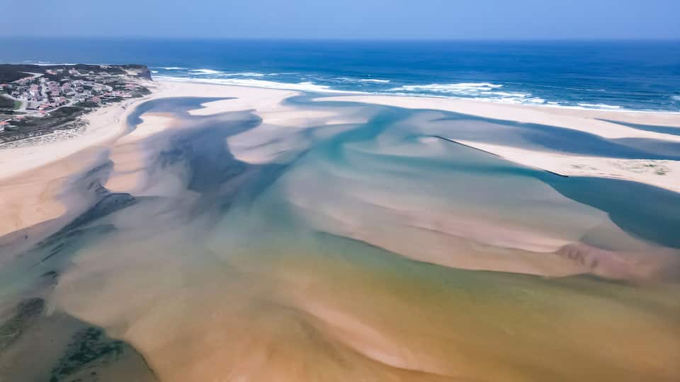 A coastal landscape with a wide sandy beach, a clear blue ocean, and a distant town.