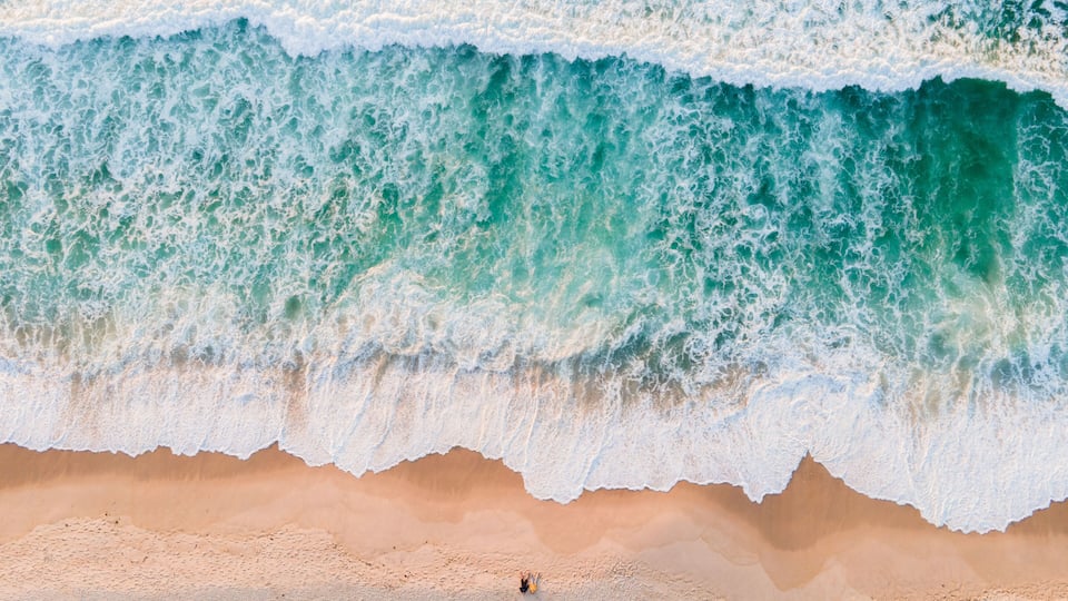 A beach with waves crashing onto the shore and a single person standing in the sand.