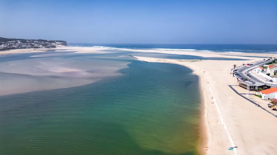 A coastal landscape with a wide sandy beach, a calm sea, and a clear sky.
